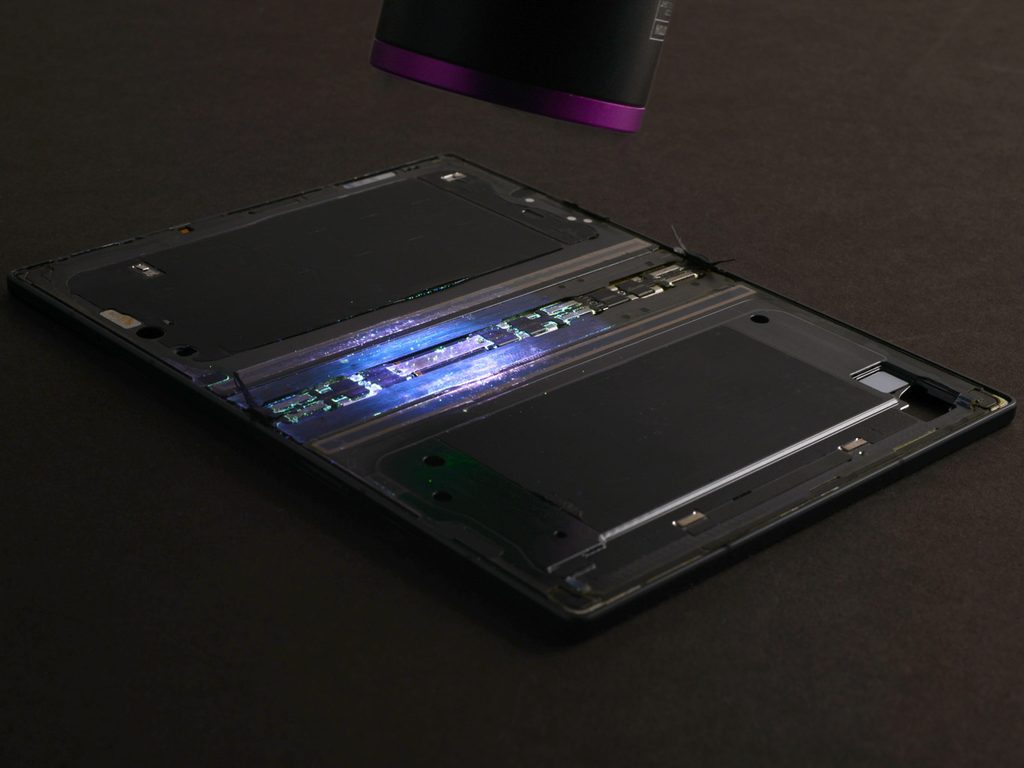 iFixitが分解したGalaxy Z Fold8の内部。ヒンジ周辺に入り込んだUV粉末が紫外線ライトで青く光っている